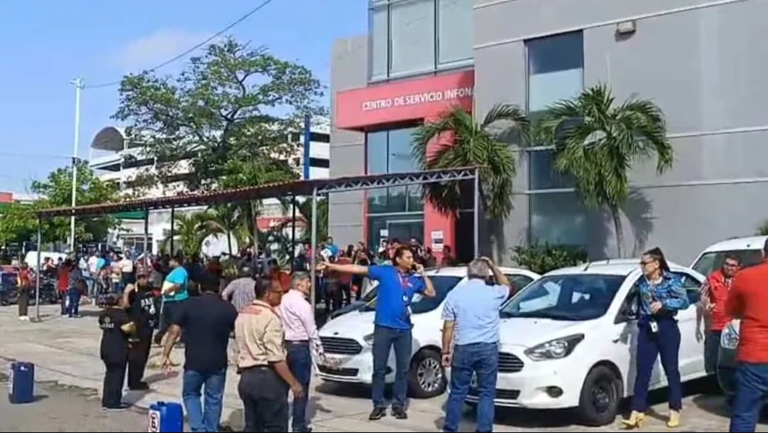 Grupo de pessoas reunido do lado de fora de um prédio após o terremoto em Chiapas, no México, com carros estacionados e equipes orientando a saída.