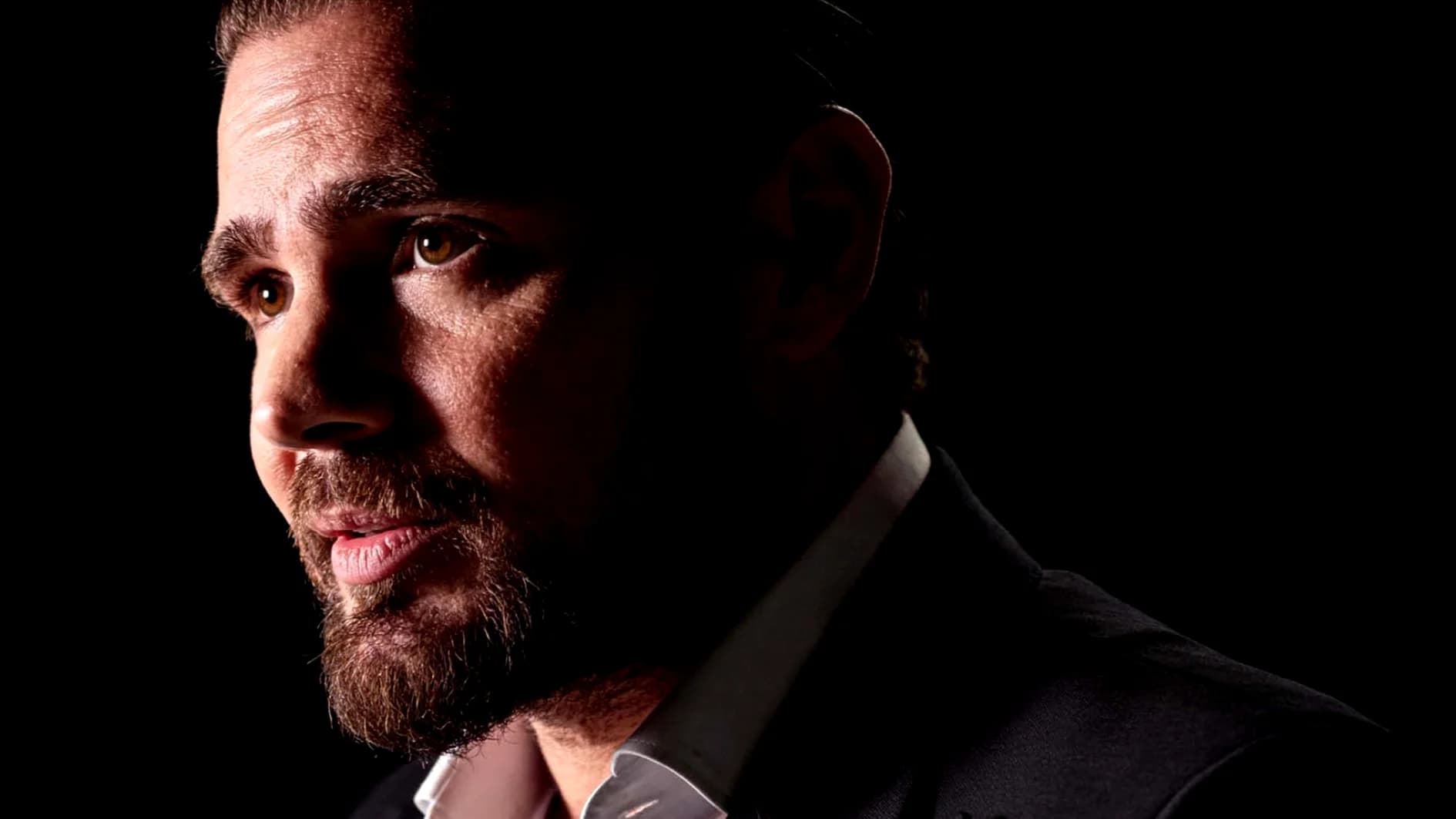 Retrato de perfil do banqueiro Daniel Vorcaro, controlador do Banco Master, em ambiente com iluminação de contraste contra fundo escuro.