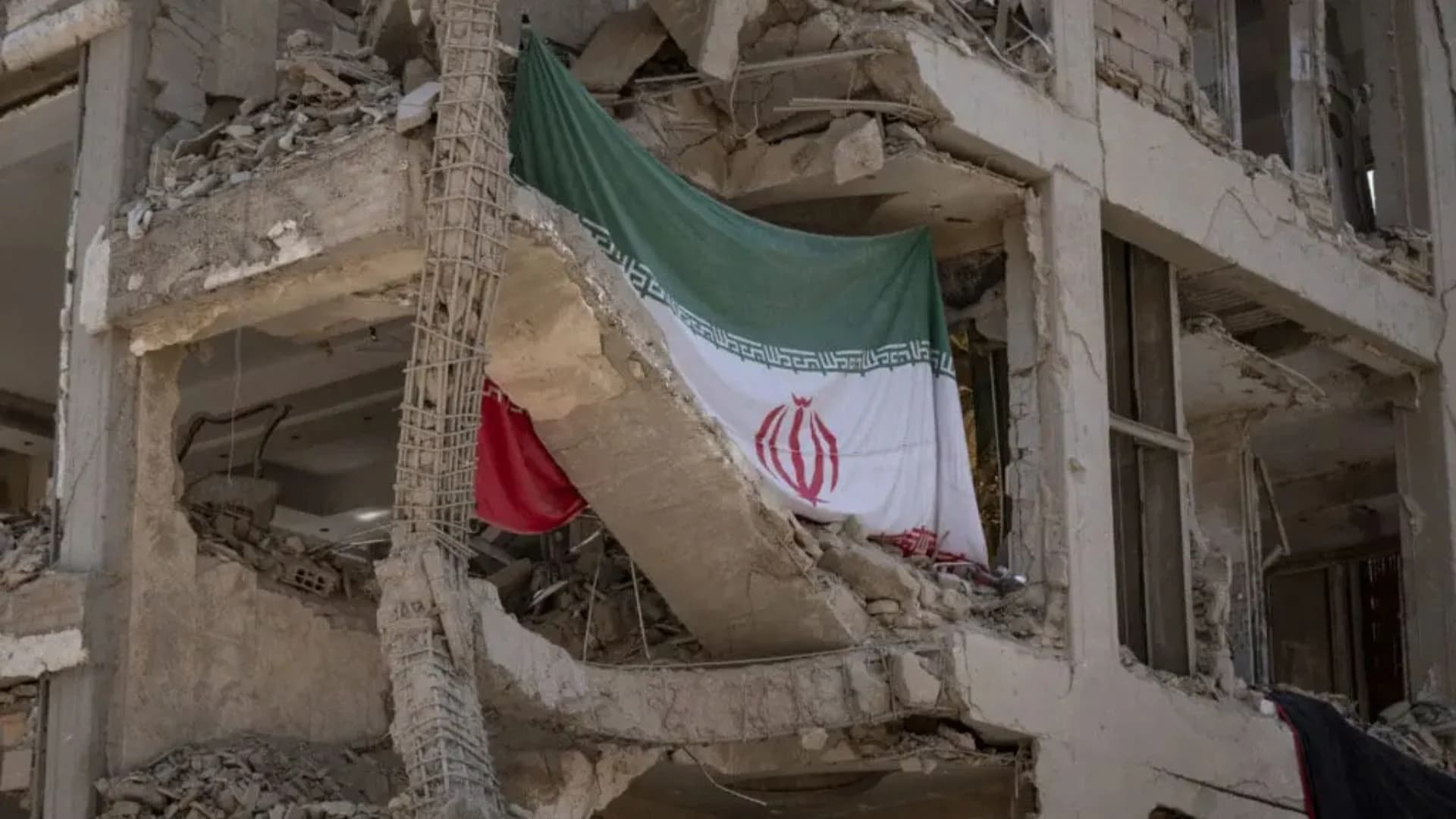 Bandeira do regime iraniano em meio aos escombros de guerra.