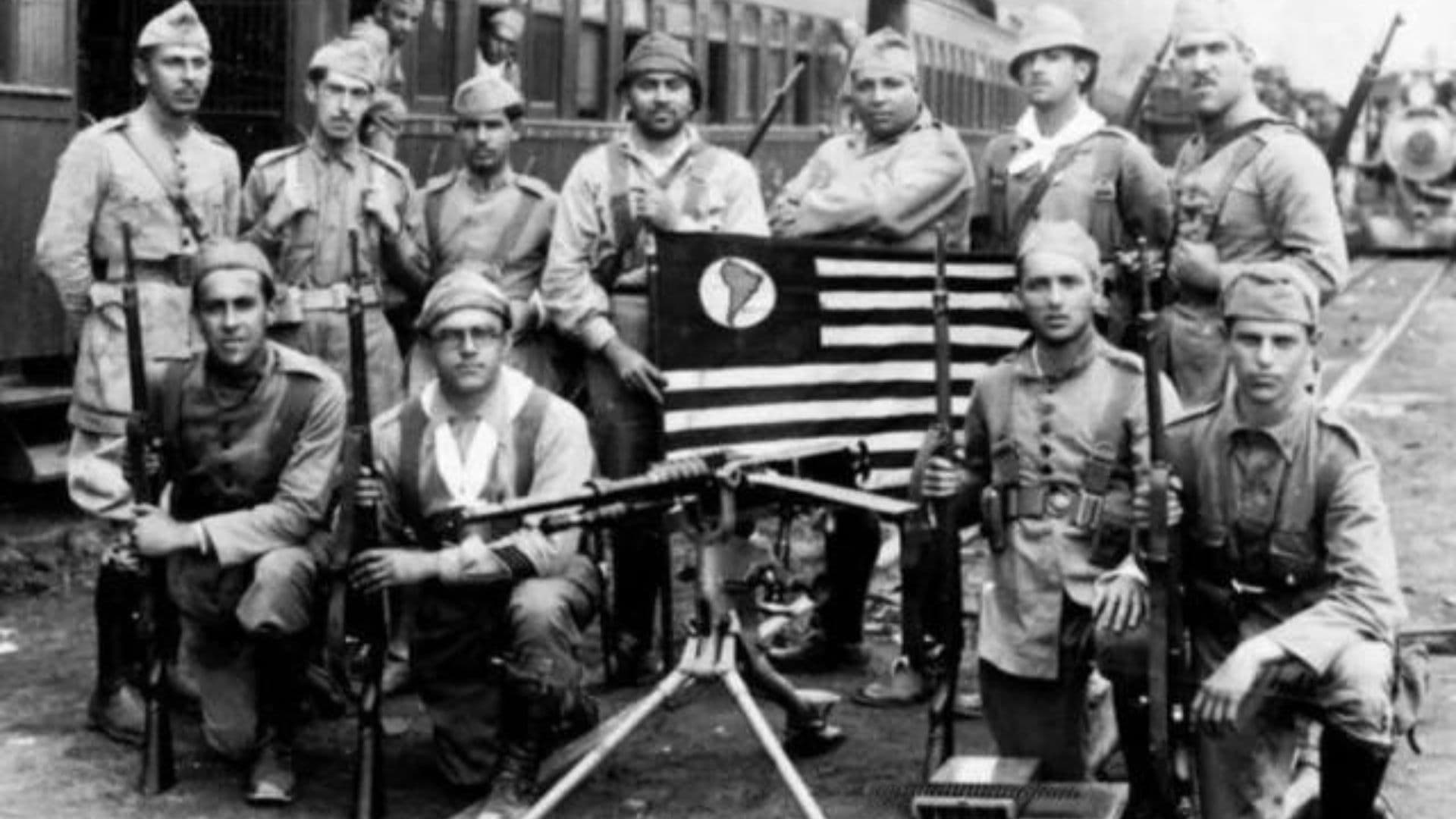 Soldados constitucionalistas posando ao lado de armamentos e da bandeira do estado