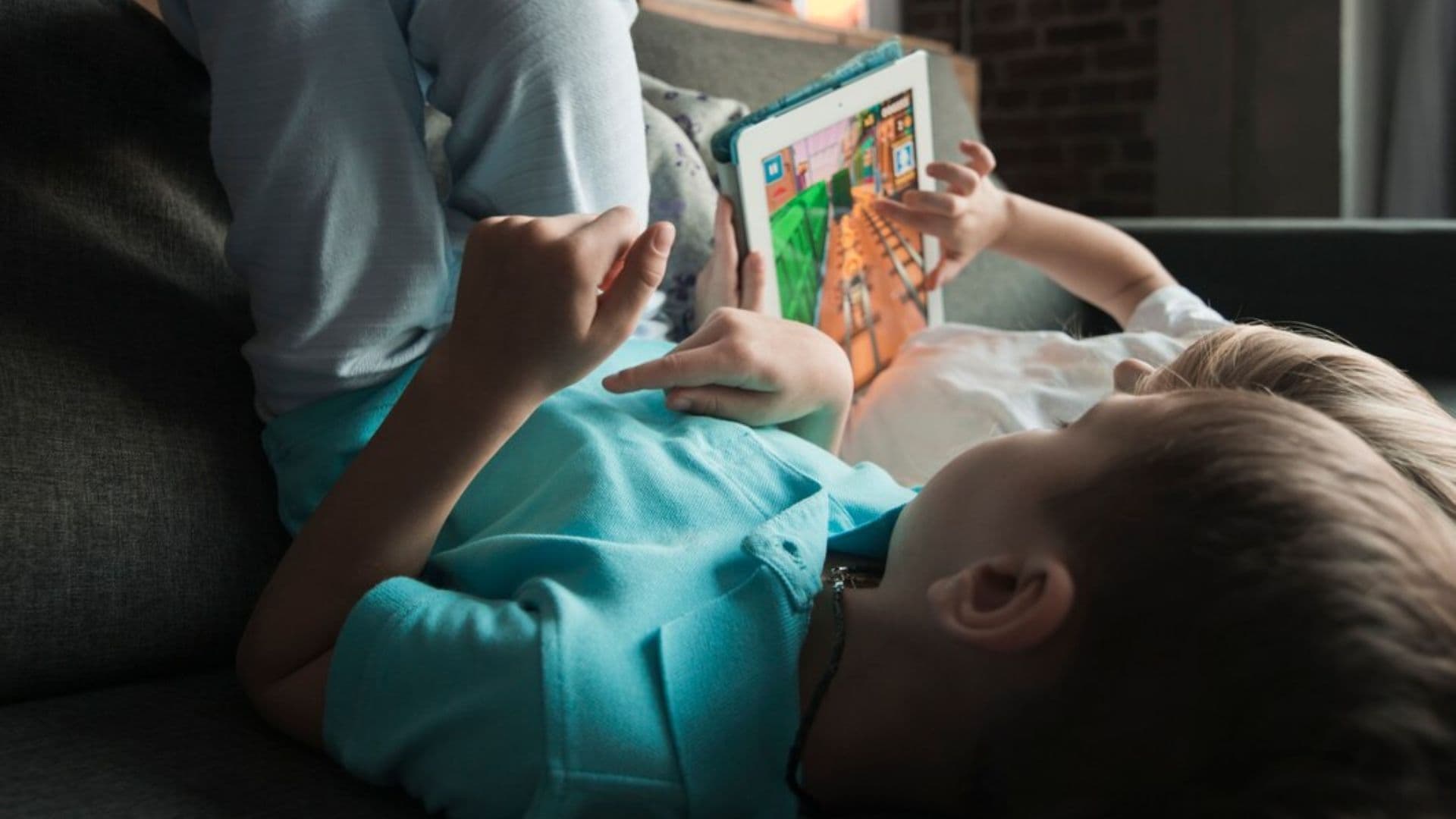 Menino mexe em tablet no escuro, enquanto está deitado na cama