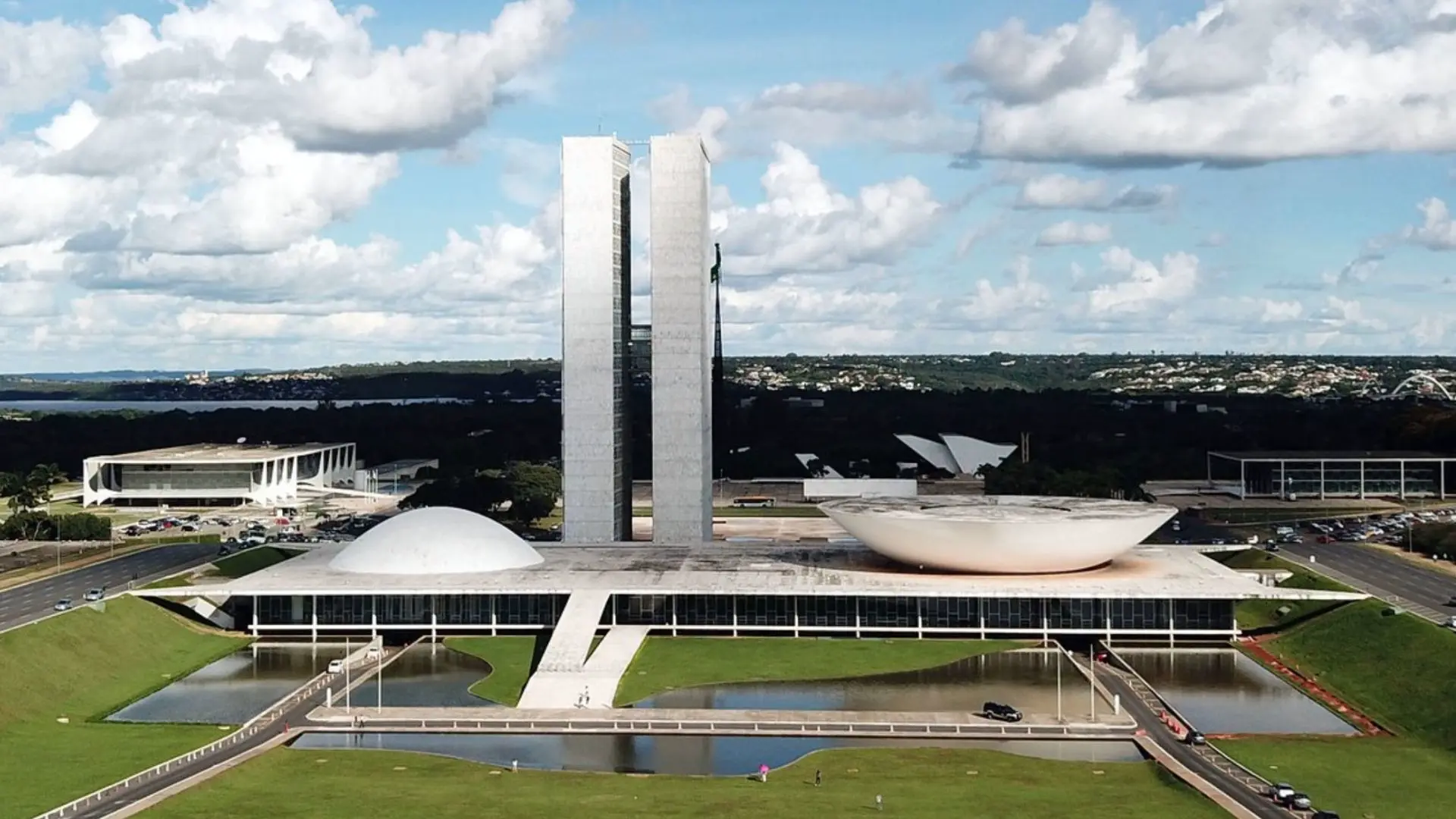 Prédio do Congresso Nacional em Brasília. O Céu está azul, com nuvens e o gramado verde