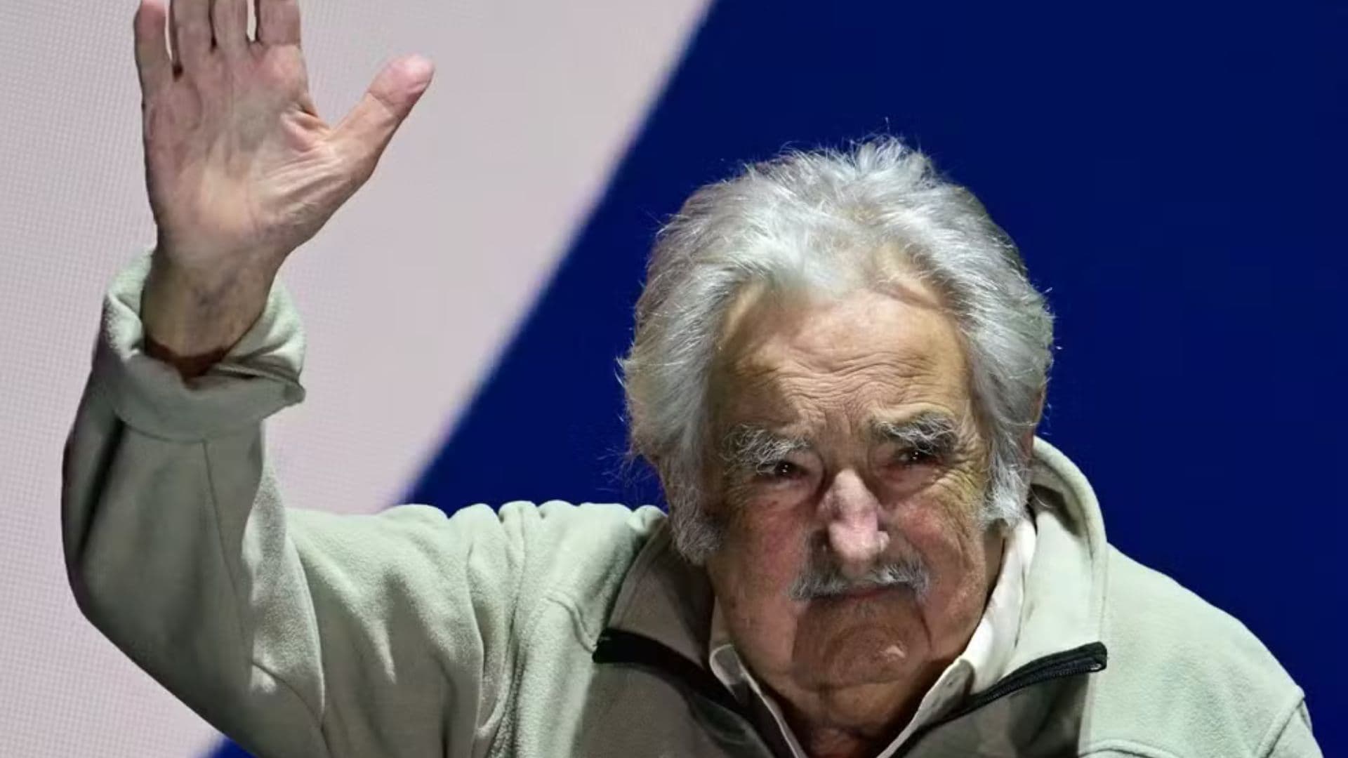 Pepe Mujica acenando em frente a uma bandeira uruguaia