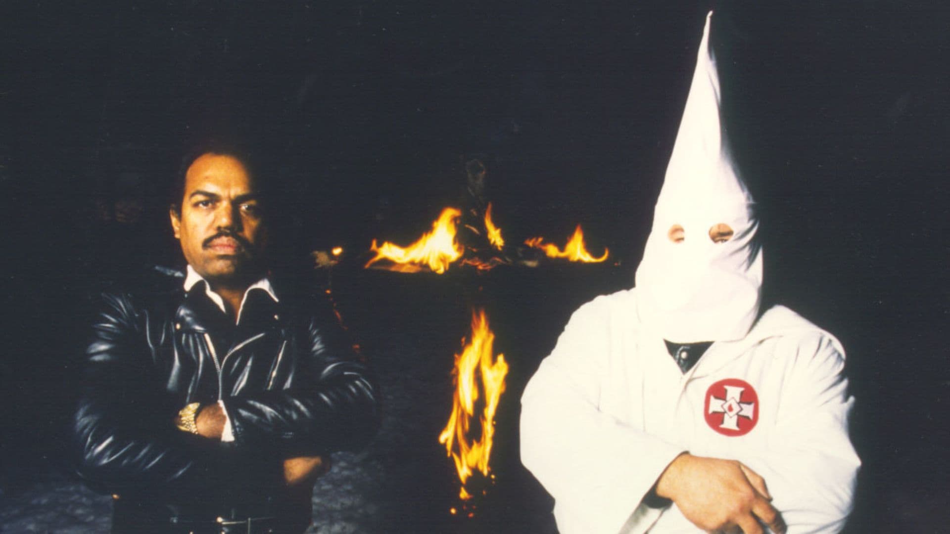 Daryl Davis dizendo ao lado de um membro da Ku Klux Klan (KKK) em frente a uma cruz pegando fogo.