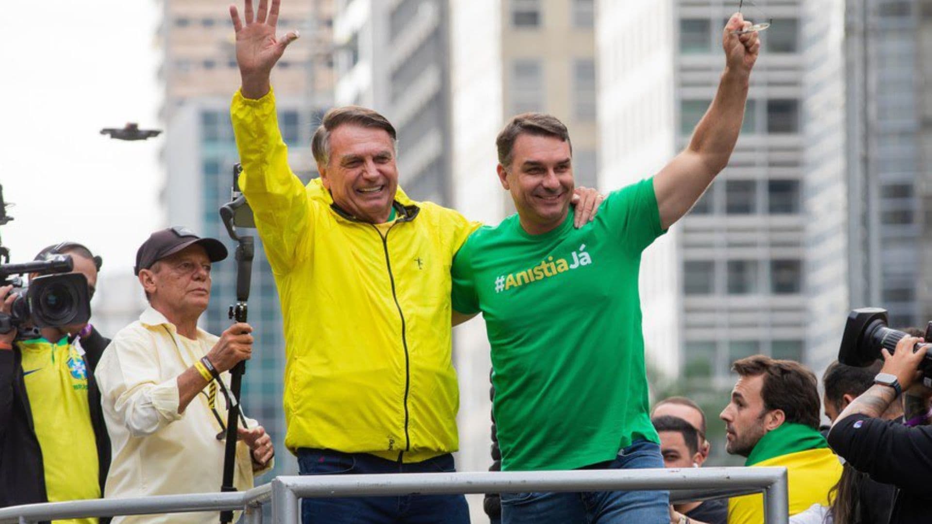 Flávio e Jair Bolsonaro se abraçam enquanto cumprimentam apoiadores durante manifestação.